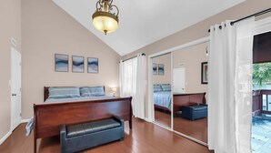 A bedroom with a wooden bed, a bench, a ceiling light, and a sliding glass door leading to a balcony. - Driftwood Days Pet Friendly Beach Home (Myrtle Beach)