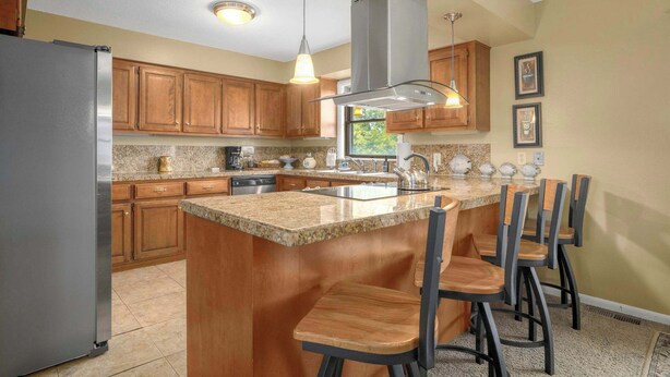 A kitchen with wooden cabinets, a granite countertop, a stainless steel refrigerator, a gas range, and a large island with bar stools. - Nature's Sanctuary-3 Mi to Downtown Eureka Springs (Eureka Springs)
