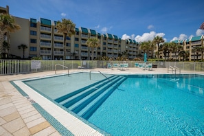 A swimming pool with clear blue water, surrounded by a white fence and palm trees.