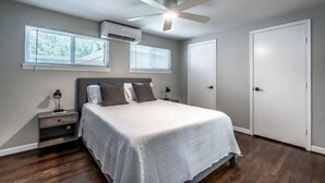 A bedroom with a bed, nightstands, an air conditioner, a ceiling fan, and a door. - Stylish 1BR Urban Retreat (Houston)