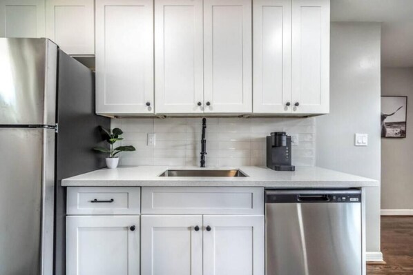 A modern kitchen with white cabinets, stainless steel appliances, and a tiled backsplash. - Stylish 1BR Urban Retreat (Houston)