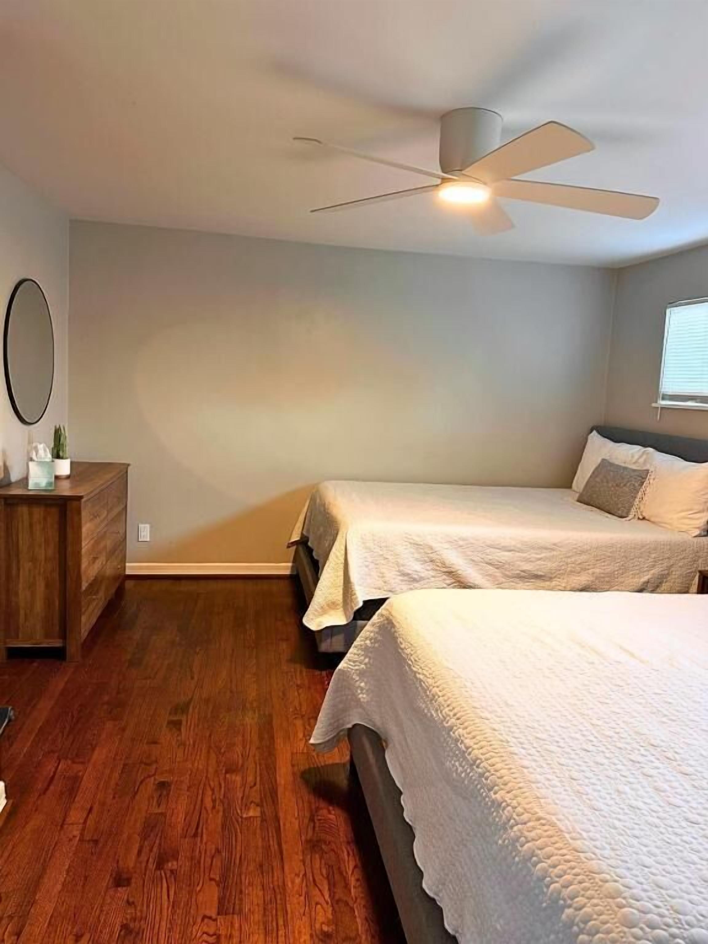A bedroom with two beds, a ceiling fan, a dresser, and a mirror.