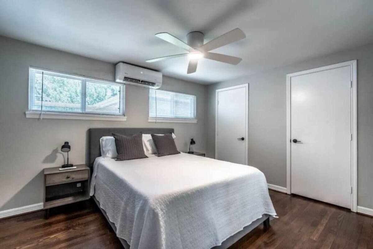 Une chambre à coucher comprenant un lit, des tables de chevet, un ventilateur de plafond et deux fenêtres équipées de stores.