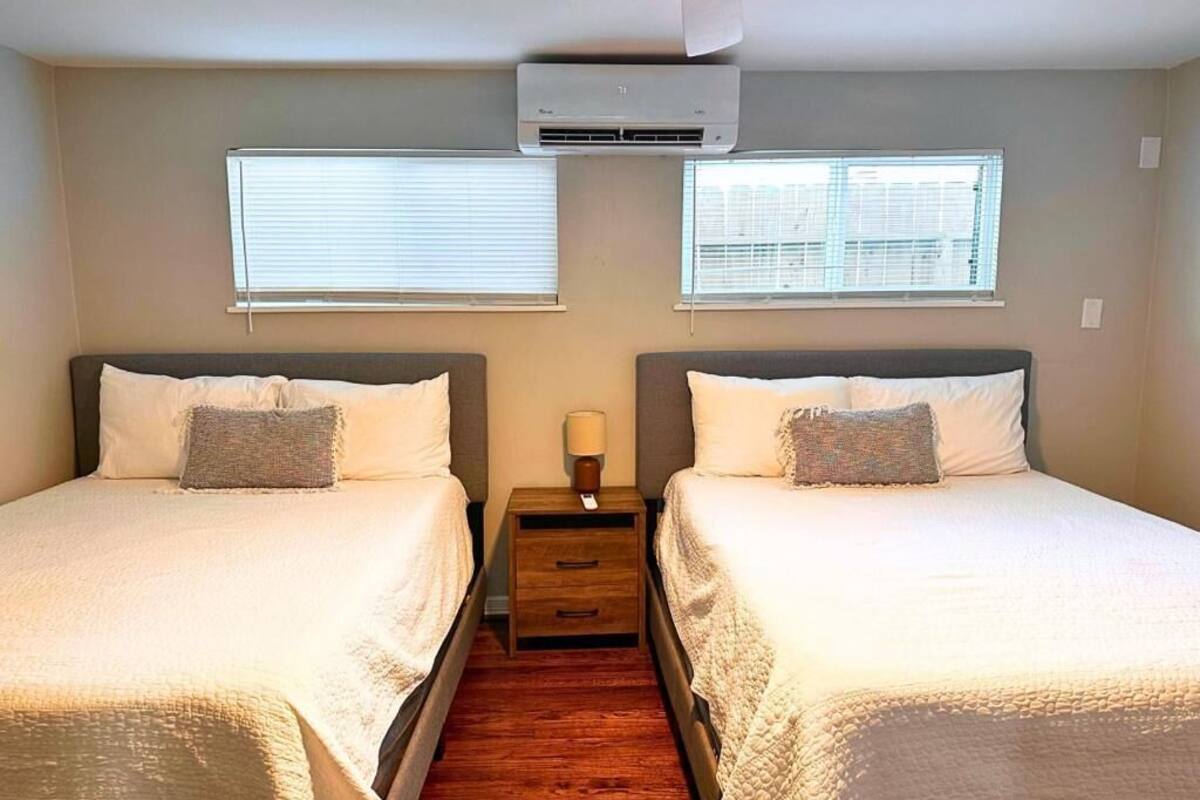 Une chambre avec deux lits, un ventilateur de plafond, un appareil de climatisation et deux fenêtres équipées de stores.