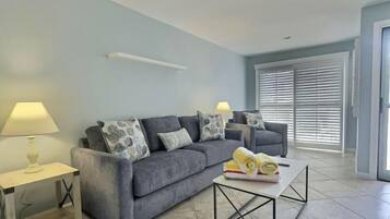 A living room with a grey sofa, two side tables with lamps, a coffee table, and a window with blinds.