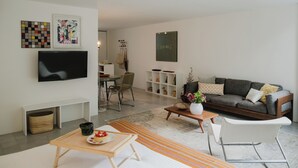 Ett modernt vardagsrum med en platt-TV, en soffa, ett soffbord och en matplats med en stol och ett litet bord.