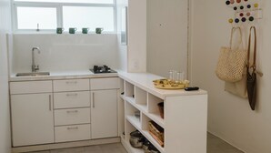 Ett kök med vita skåp, en diskho och ett fönster ovanför bänkskivan. Det finns hyllor med olika föremål och ett väggmonterat ställ med färgglada bollar.