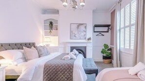 Ein Schlafzimmer mit einem großen Bett, einem Einzelbett, einem Kamin, einer Hängelampe und einem Fenster mit Jalousien.
