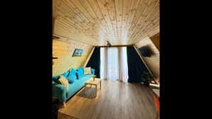 Une pièce mansardée chaleureuse avec un plafond en bois, un canapé de couleur turquoise, une petite table et une fenêtre avec des rideaux.