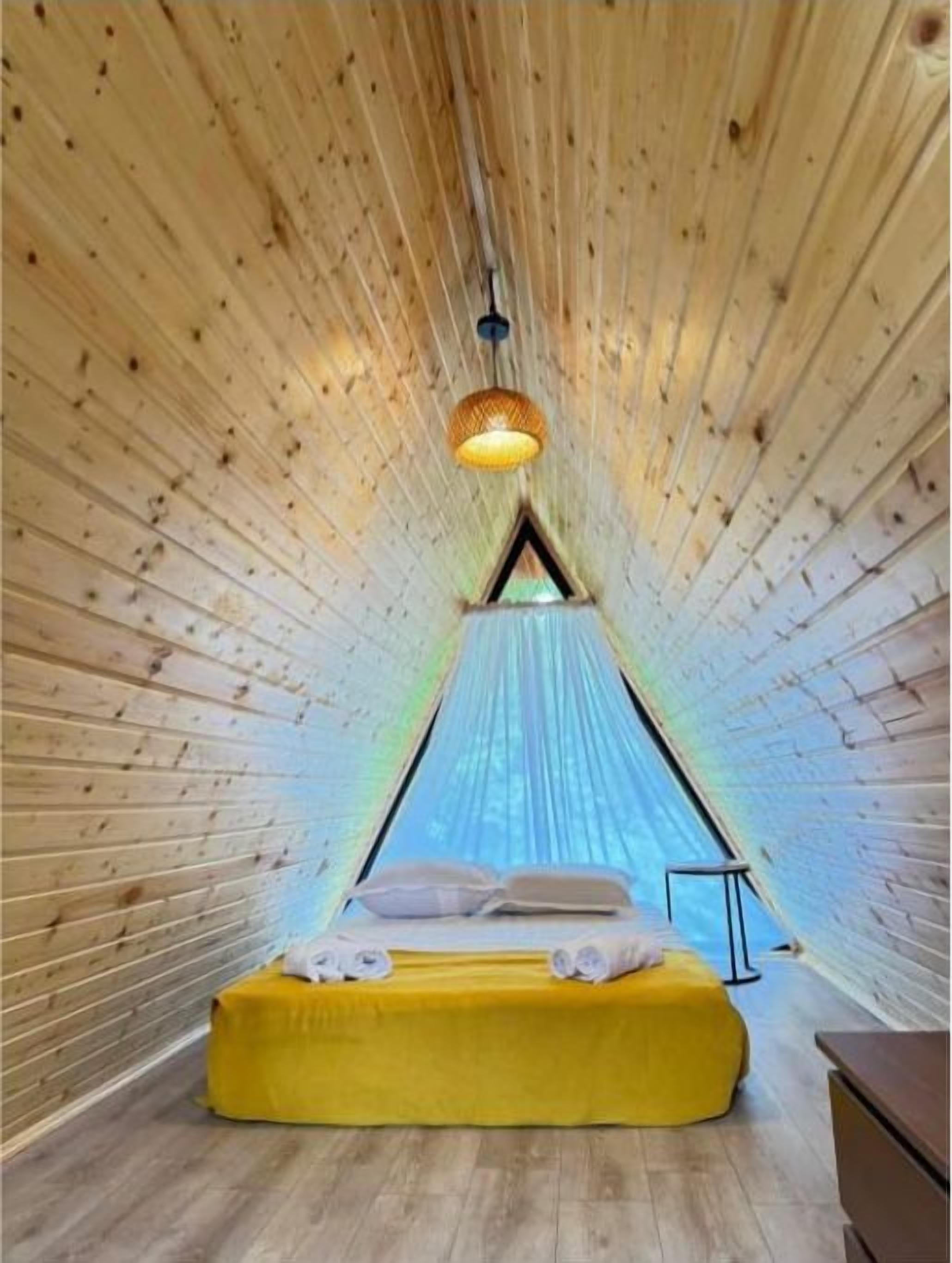 Een kamer met een bed, een hangende lamp en een schuin houten plafond.