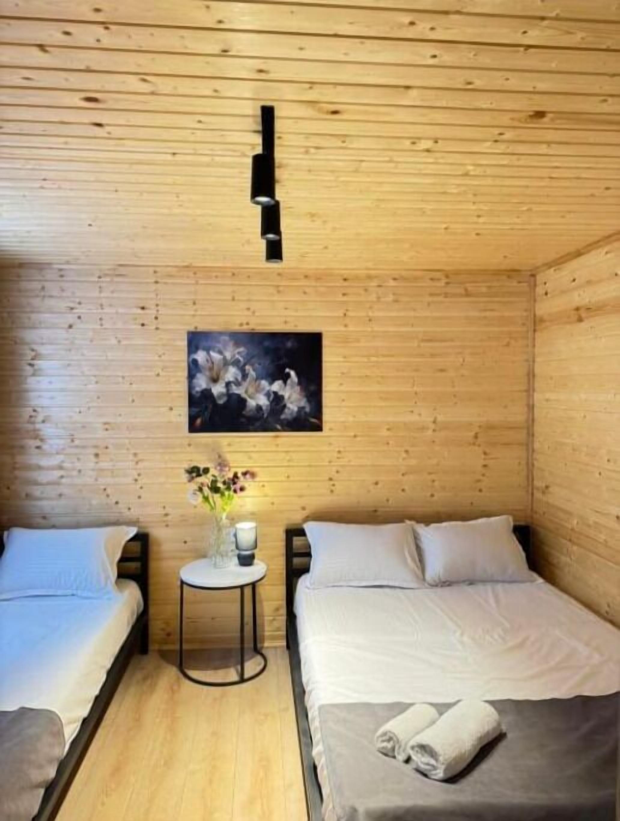 Una habitación acogedora de estilo cabaña con dos camas, una mesita con un florero y un cuadro en la pared.