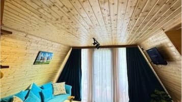 Acogedor cuarto ático con techo de madera, un sofá color esmeralda, una mesita y una ventana con cortinas.