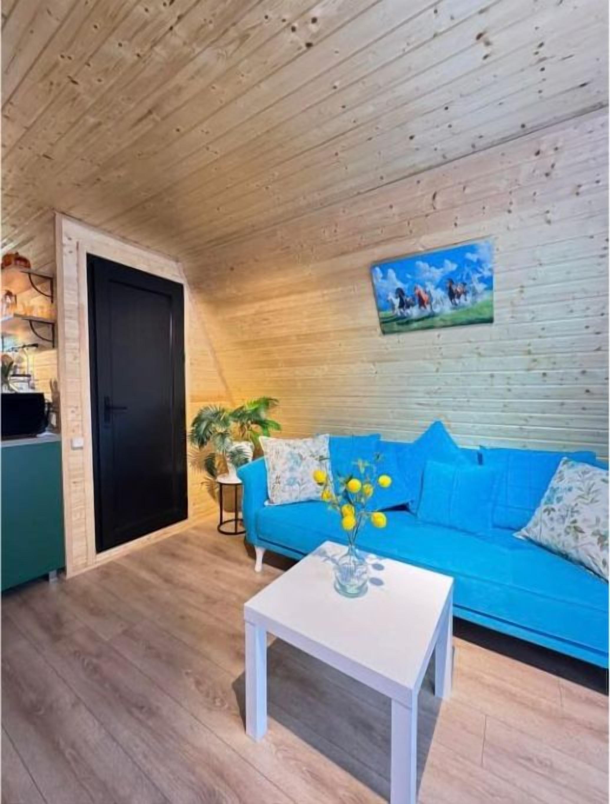 Una habitación con techo de madera, un sofá azul, una mesa de centro blanca y una puerta que da a otra estancia.
