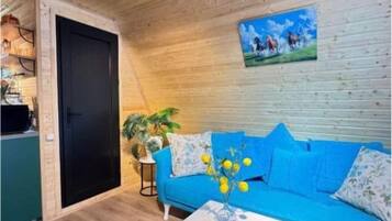 Una habitación con techo de madera, un sofá azul, una mesa de centro blanca y una puerta que da a otra estancia.