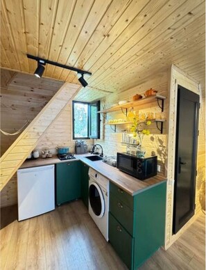 A compact kitchen with wooden beams, a washing machine, and a microwave. - Romantic Forest A-Frame • 2BR by the Sea (Tsikhisdziri)