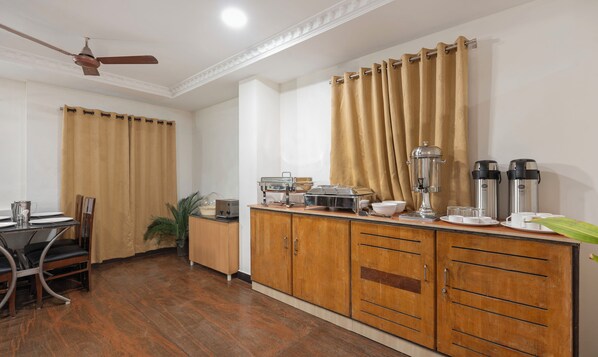 A hotel room with a wooden cabinet, a dining table with chairs, a ceiling fan, and a window with curtains.