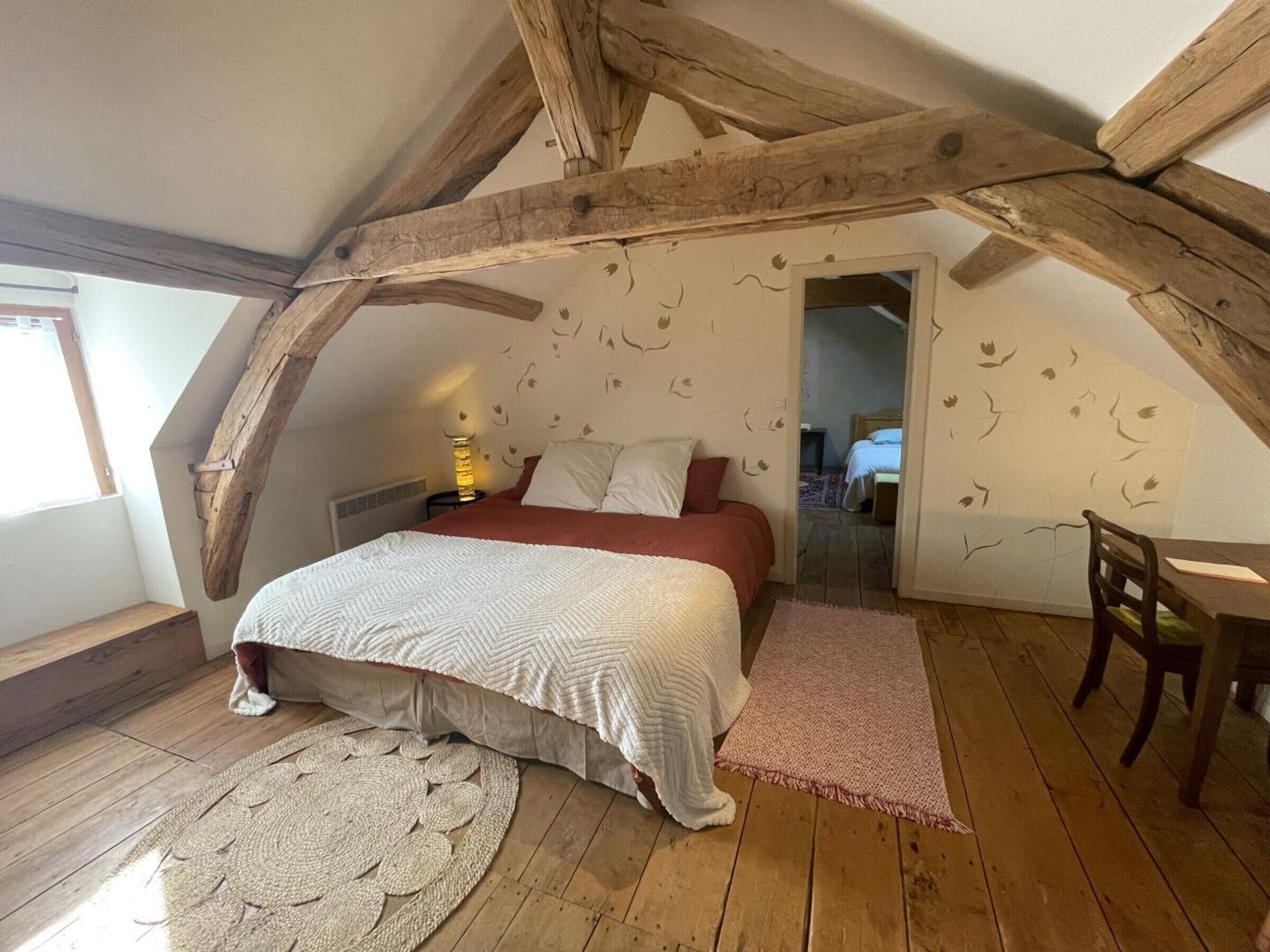 Camera da letto con soffitto spiovente, travi in legno, letto con biancheria bianca, un tavolino e una sedia.