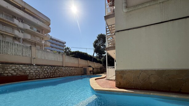 A swimming pool with clear blue water, surrounded by stone walls and a white building with balconies. - Bright Salou Apartment - 2 Bedroom, Free WiFi (Salou)