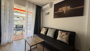 A living room with a black leather sofa, a wooden coffee table, a large window with sheer curtains, and a painting of a lioness on the wall. - Bright Salou Apartment - 2 Bedroom, Free WiFi (Salou)