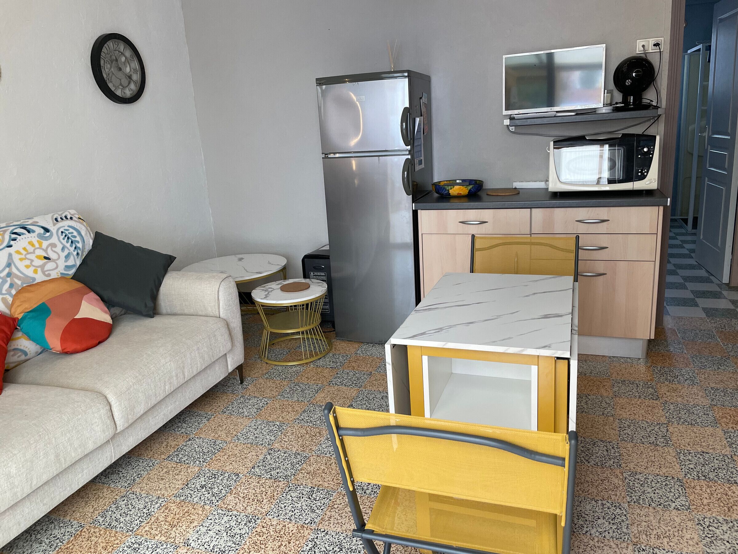 A compact living space with a sofa, a small round table, a kitchenette with a refrigerator, microwave, and a TV.