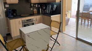 Een kleine keuken met houten kastjes, een inbouwoven en een eethoek met een tafel en stoelen.
