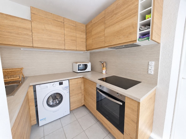 A compact kitchen with wooden cabinets, a microwave, a washing machine, and a sink.