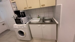 Eine kleine Küche mit Waschmaschine, Kaffeemaschine und Spüle.