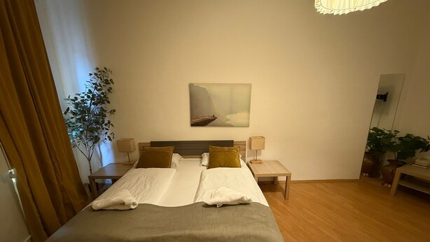 Ein Hotelzimmer mit einem großen Bett, zwei Nachttischen, einer Stehlampe, einem Bild an der Wand und einer Topfpflanze.