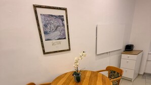 Ein Essbereich mit einem runden Holztisch, vier Stühlen, einer Topfpflanze und einem gerahmten Bild an der Wand.
