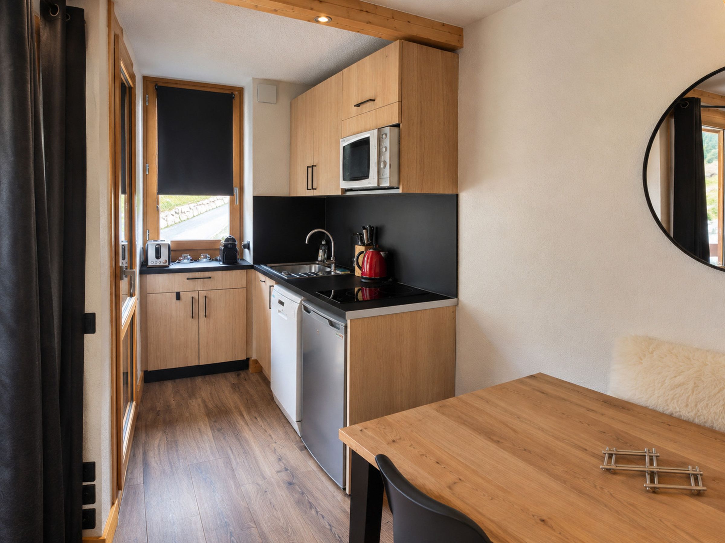 A compact kitchen with wooden cabinets, a microwave, a kettle, and a sink.