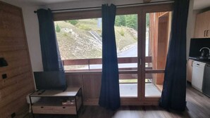 A room with a wooden floor, a small table with a box, a window with curtains, and a view of a hillside. - Renovated Studio for 4 in Plagne Bellecôte, balcony (Plagne Bellecôte)
