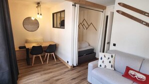A cozy room with a wooden floor, a sofa with a ski-themed pillow, a dining table with chairs, and a bed with curtains. - Renovated Studio for 4 in Plagne Bellecôte, balcony (Plagne Bellecôte)