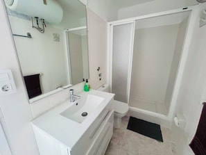 Ein Badezimmer mit einem weißen Waschbecken, einem Spiegel, einer Dusche und einer schwarzen Matte.