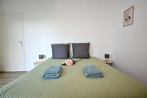 Una cama bien hecha con dos almohadas, un florero con flores y dos toallas dobladas sobre la cama.