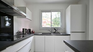 A modern kitchen with white cabinets, a black countertop, a stainless steel range hood, a window with a view of trees, and a built-in sink. - Modern house with garden, not overlooked – 3 bedrooms – Vannes (Vannes)