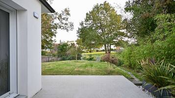 A modern house with a concrete patio, a well-maintained lawn, and a variety of trees and shrubs.