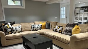 Ein Ecksofa mit vielen Kissen, einem schwarzen Couchtisch und einem hellen Holzboden.