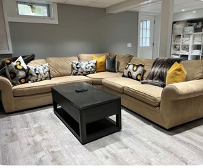 Ein Ecksofa mit vielen Kissen, einem schwarzen Couchtisch und einem hellen Holzboden.