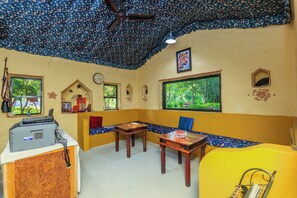 A room with a ceiling fan, a table with a bowl, a bench, and a window with a view of greenery.