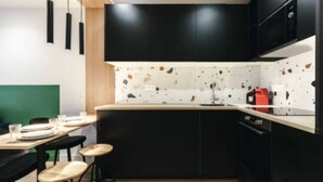 A modern kitchen with black cabinets, a white speckled backsplash, and a wooden countertop. - Cosy apartment: 2-minute walk from PSG & Roland-Garros (Boulogne-Billancourt)