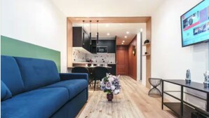 A modern living room with a blue sofa, a wooden coffee table with a vase of flowers, and a kitchen in the background. - Cosy apartment: 2-minute walk from PSG & Roland-Garros (Boulogne-Billancourt)