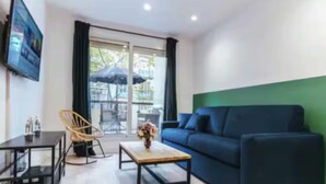 A modern living room with a blue sofa, a wooden coffee table, a black TV on the wall, and a dining area with a table and chairs. - Cosy apartment: 2-minute walk from PSG & Roland-Garros (Boulogne-Billancourt)