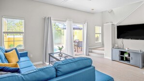 Een woonkamer met een blauwe bank, een glazen salontafel, een grijze tv-kast en een flatscreen televisie.