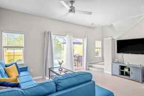 A living room with a blue sofa, a glass coffee table, a grey entertainment unit, and a flat-screen TV.