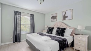 Een slaapkamer met een bed, twee nachtkastjes, een raam met gordijnen en twee aan de muur hangende foto's.