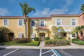 A yellow building with white shutters, a wheelchair-accessible entrance, and a palm tree. - Spacious townhouse w/ pool, patio & workspace (Kissimmee)