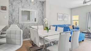 Een moderne woonkamer met een marmeren wand, een blauwe bank, witte stoelen en een eettafel.