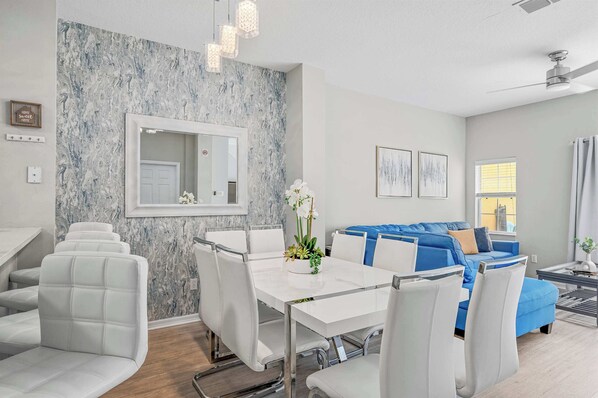 A modern living room with a marble wall, a blue sofa, white chairs, and a dining table.