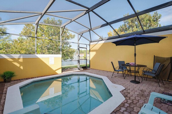 A covered outdoor swimming pool with a glass ceiling, yellow walls, and a table with chairs. - Spacious townhouse w/ pool, patio & workspace (Kissimmee)