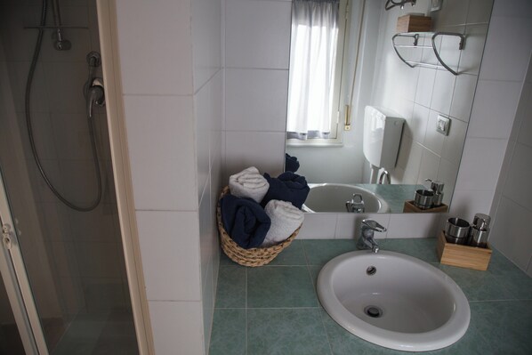Un baño con ducha, lavamanos, espejo y una cesta de toallas.